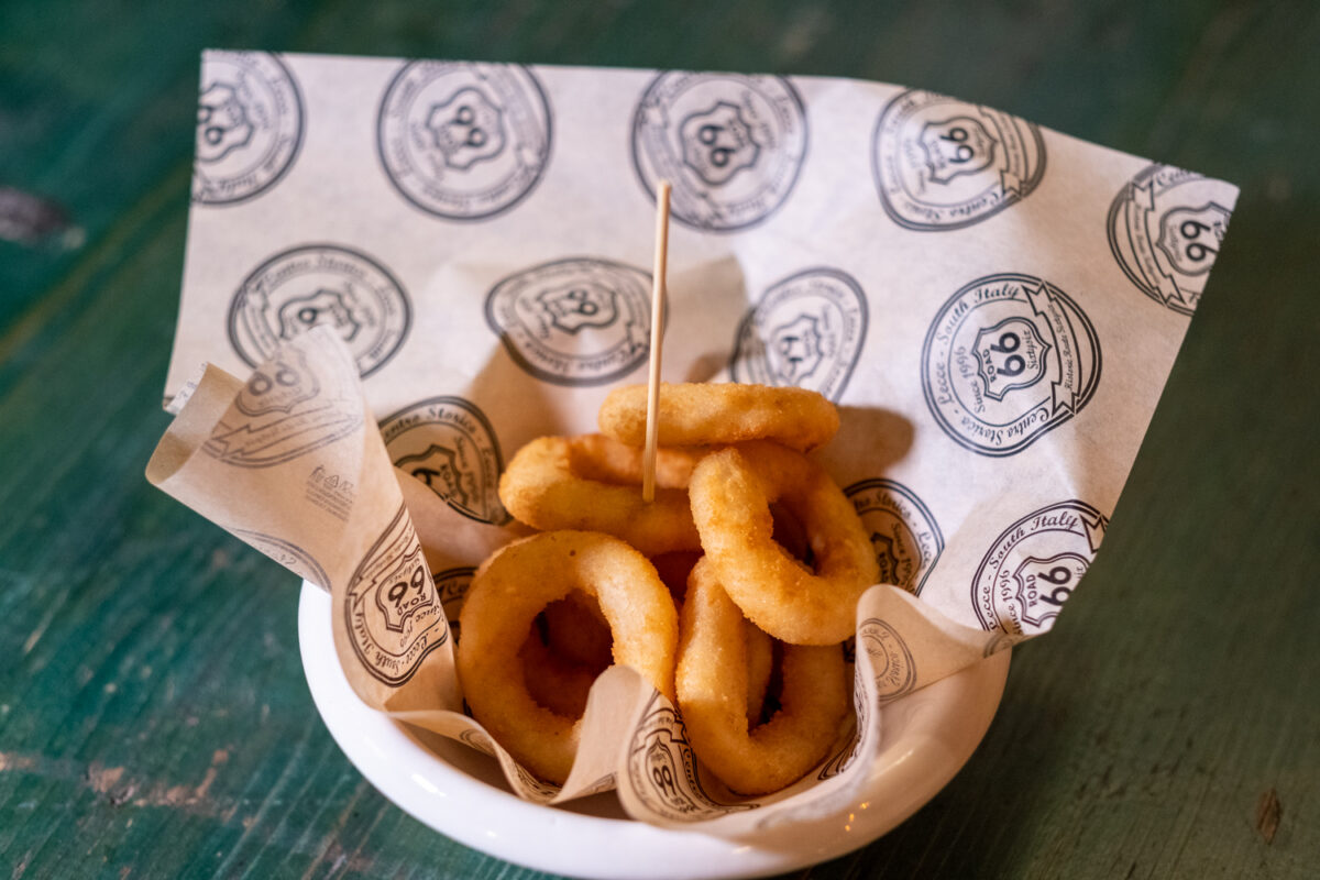 Anelli di cipolla fritti in pastella dentro una ciotola foderata con la carta stampata Road 66