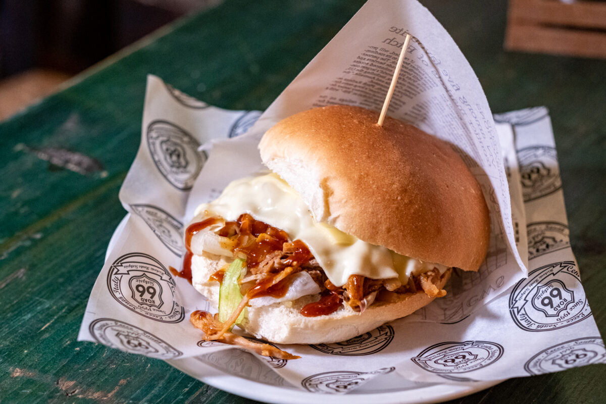 Panino con pulled pork, salsa barbecue e provola fusa, appoggiato sulla carta del Road 66
