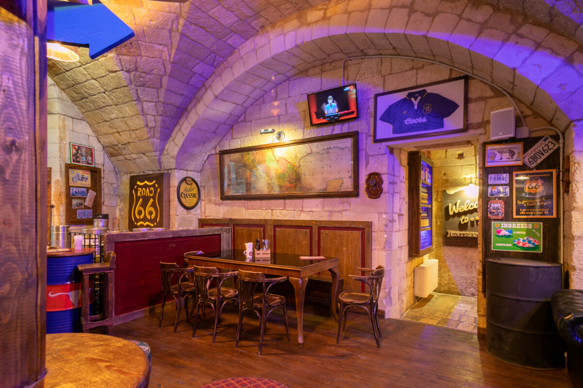 Sala del Road 66 illuminata di viola con una grande mappa incorniciata, l'insegna al neon Road 66 e una maglia da calcio appesa