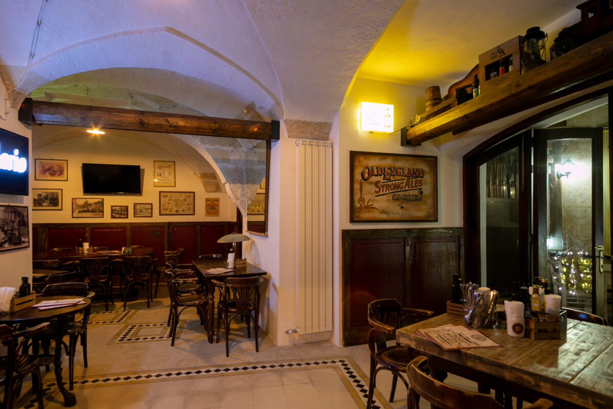 Sala del Road 66 con volte a crociera, boiserie bordeaux, stampe alle pareti e l'insegna Old England Strong Ales